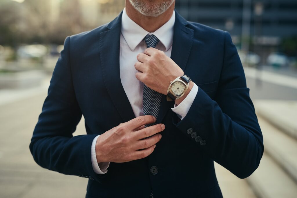 Mann im Anzug, der seine Krawatte im Freien in Hamburg zurechtrückt, trägt eine Uhr und ein weißes Hemd - das Gesicht ist nicht zu sehen. Perfektes Beispiel für Herrenausstatter Eleganz und Maßanzüge Handwerkskunst.