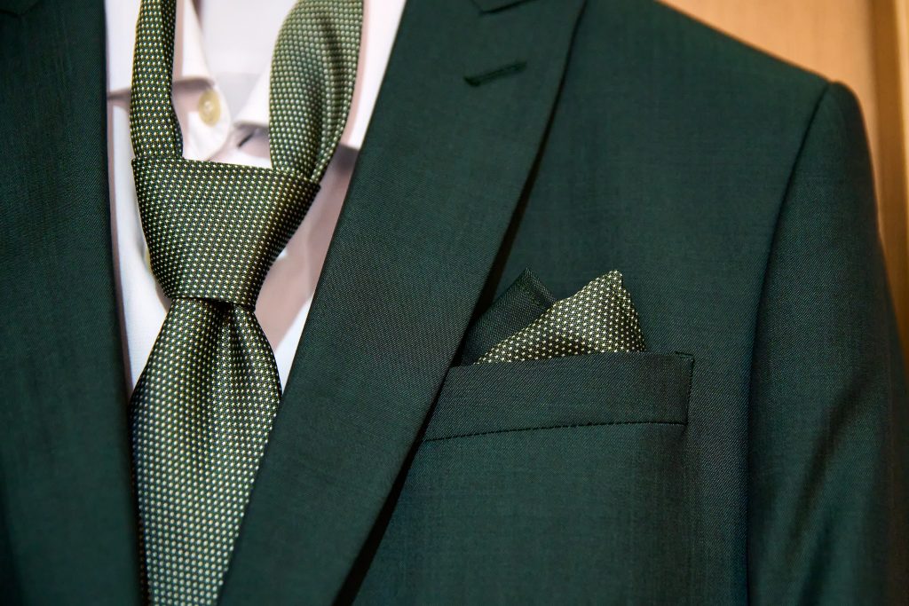 Ein dunkelgrüner italienischer Hochzeitsanzug hängt zusammen mit einem weißen Hemd und einem hellgrünen Einstecktuch.